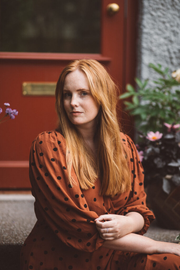 Porträtt av illustratören Lina Schnaufer framför en röd dörr i Majorna, Göteborg